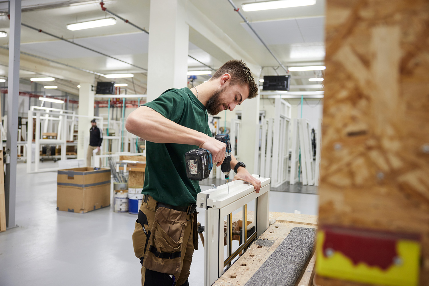 Jakob, som arbejder i produktion, skruer en skrue i et vindue.