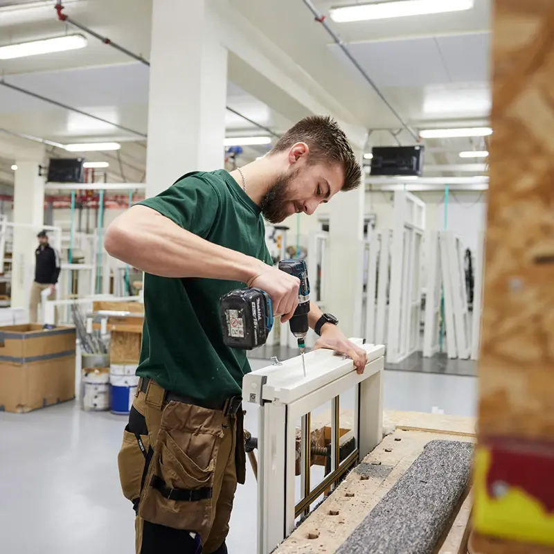 Jakob, som arbejder i produktion, skruer en skrue i et vindue.