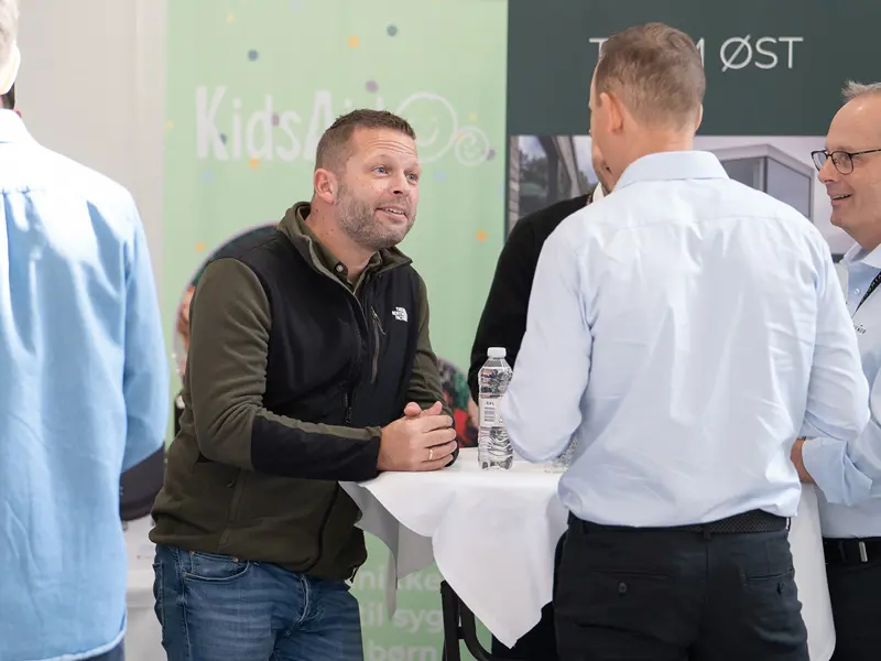 Åben Fabrik 2025 - ivrige sælgere omkring et cafebord med KidsAid i baggrunden.