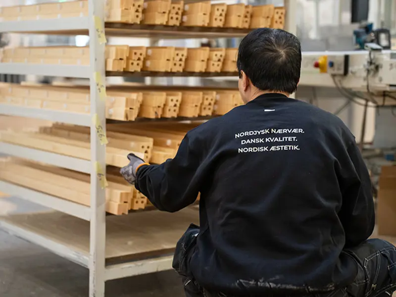 Medarbejder i produdktionen sidder på hug med ryggen til og kigger på pinde fra CNC.