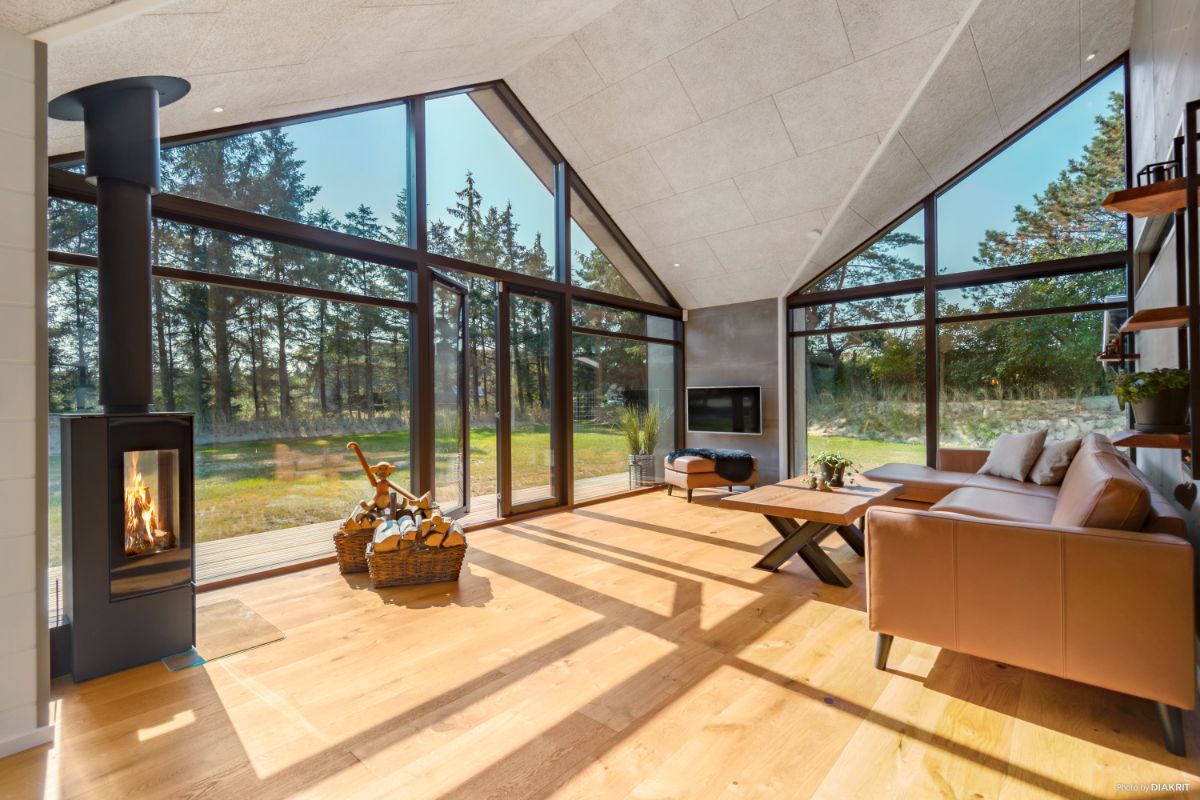 Stenhøj Husene designlinje Nord Line. Indvendig fra stuen med pejs af store vinduer og døre i sort.