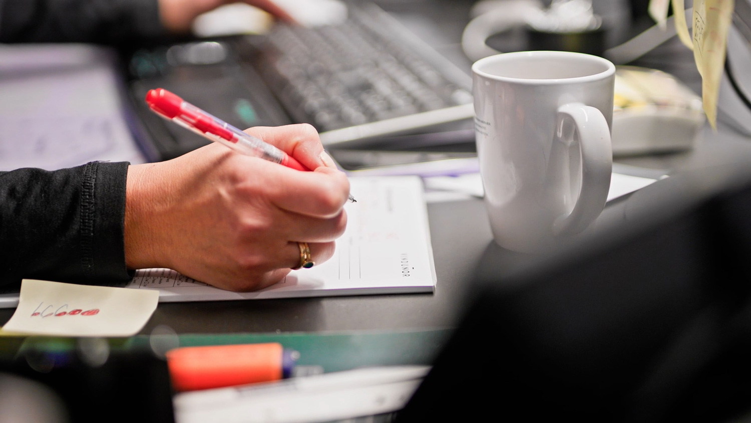 En hånd der holder en kuglepen, som er ved at skrive på en blok.
