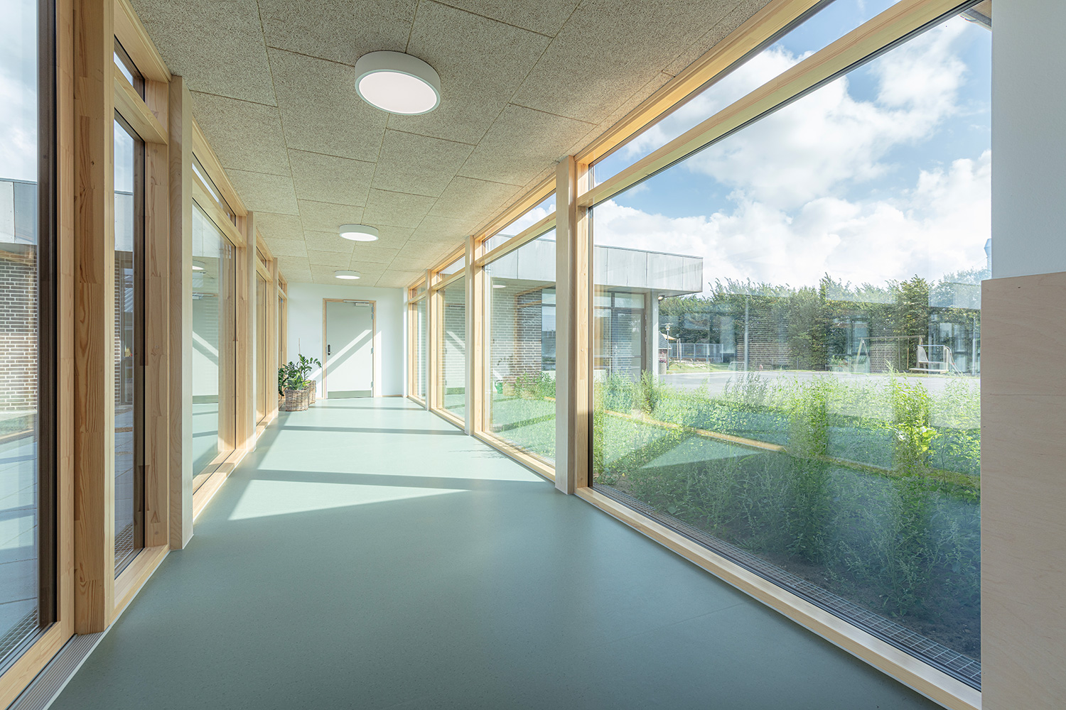 Lys skolegang med glaspartier på begge sider hele vejen igennem, lavet i lakeret fyrretræ - reference Muldbjergskolen