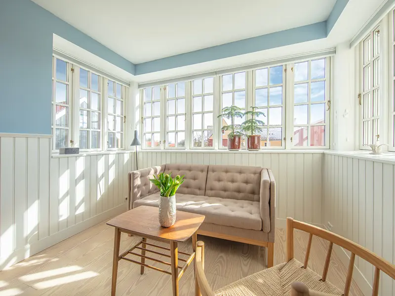 sofa hjørne med vinduesparti over sofaen. det er med sidehængt vinduer med bondehus sprosser g i farven hvid