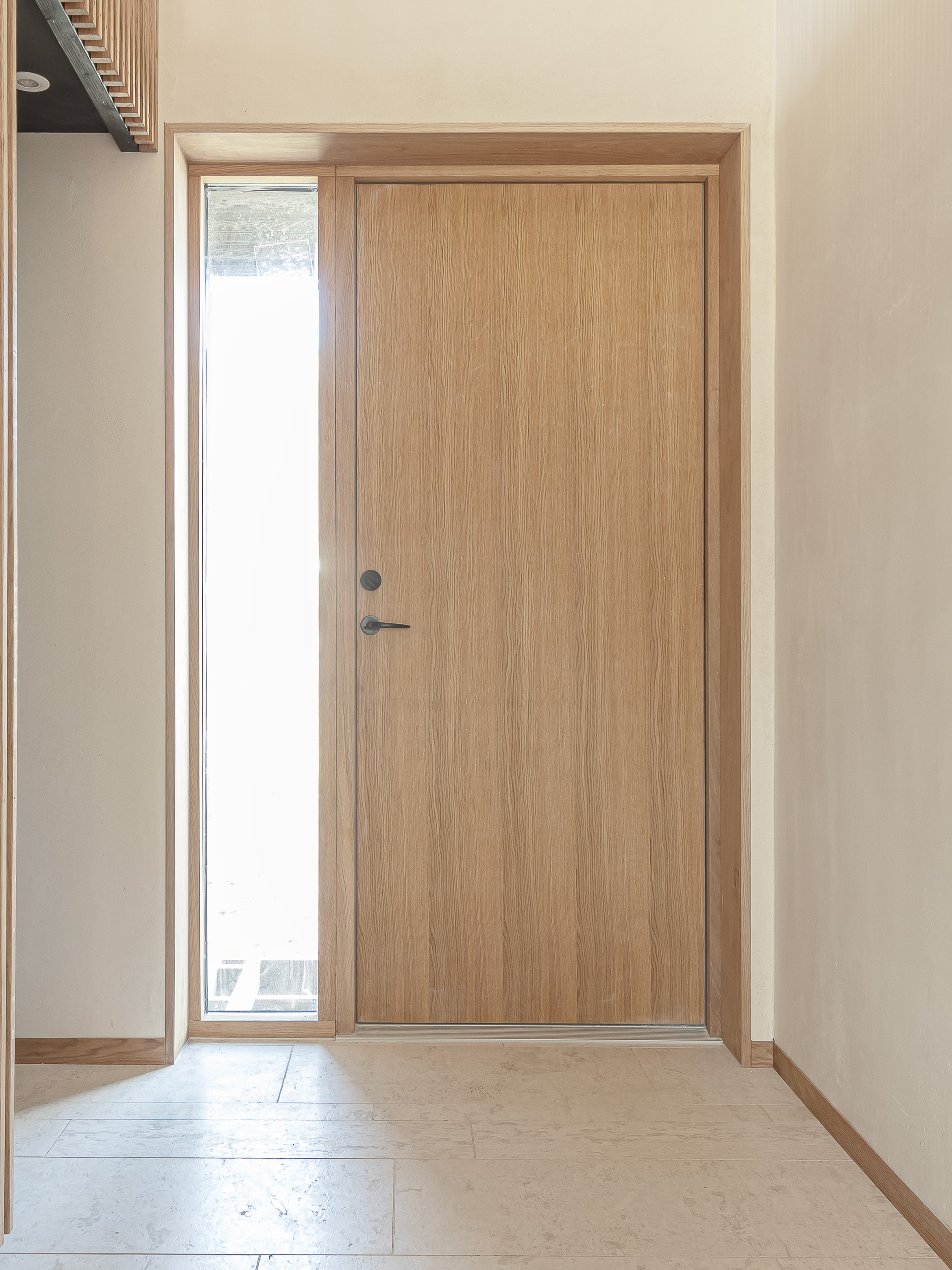 Facadedør i olieret egetræ med et lille sideparti, der giver et diskret lysindfald. 