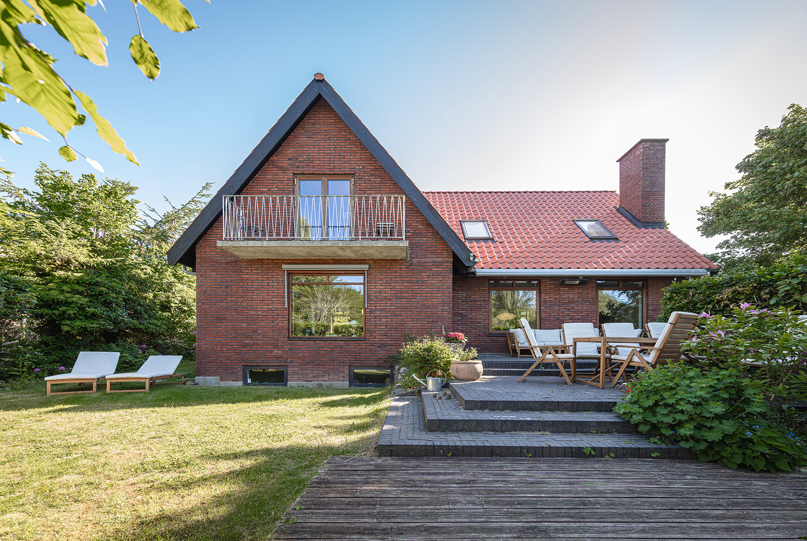 Mahogni-vinduer, Nor1, i murstenshus med kvist, ovenlysvinduer og terrasse i baggrunden.