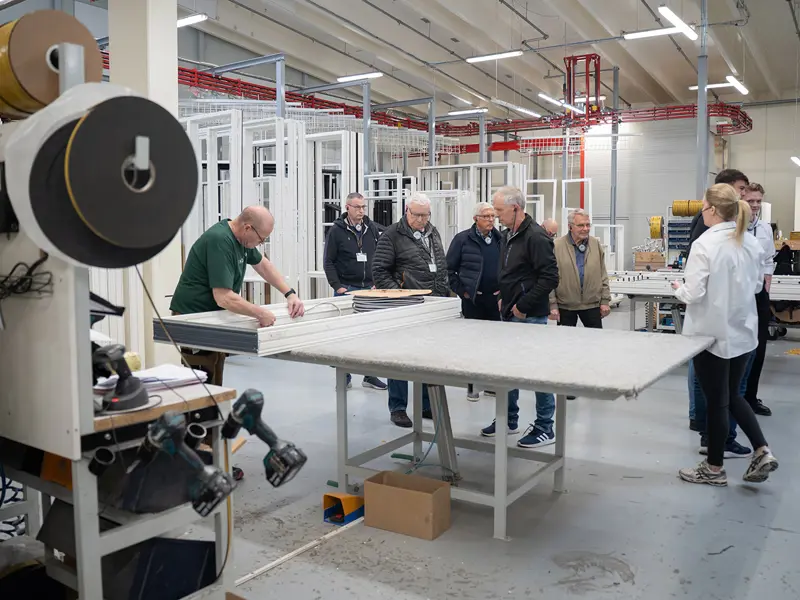 Åben Fabrik 2025 - 6 gæster på rundvisning og Caroline viser rundt. En medarbejder lægger tætningsbånd i.